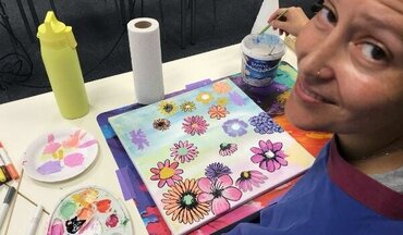 Farbraum_onkologisches_Kunstprojekt_Universitätsmedizin_Göttingen_Blumen Das Bild ist im Rahmen des onkologischen Kunstprojektes "farbRaum" der Universitätsmedizin entstanden und zeigt eine Patientin, die gerade ein buntes Bild mit vielen Blumen malt und in die Kamera lächelt.