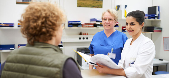 Eine Ärztin und eine Krankenschwester im Gespräch mit einer Patientin.
