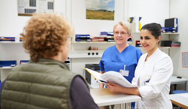 Eine Ärztin und eine Krankenschwester im Gespräch mit einer Patientin.